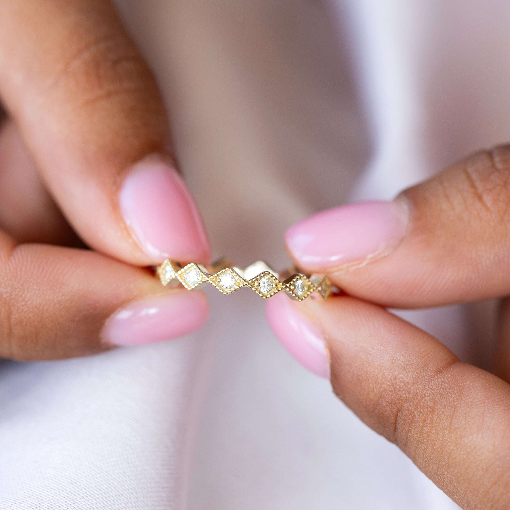 טבעת יהלומים שורה בזהב צהוב מוחזקת על יד אצבעות של אישה