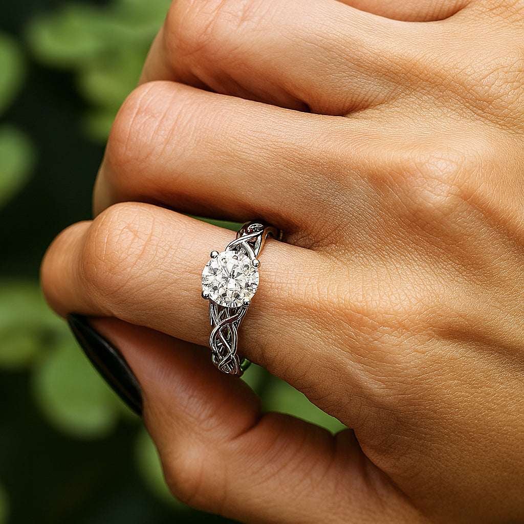 יד של אישה שעונדת טבעת אירוסין זהב לבן קלטית משובצת מוסונייט על רקע ירוק מטושטש