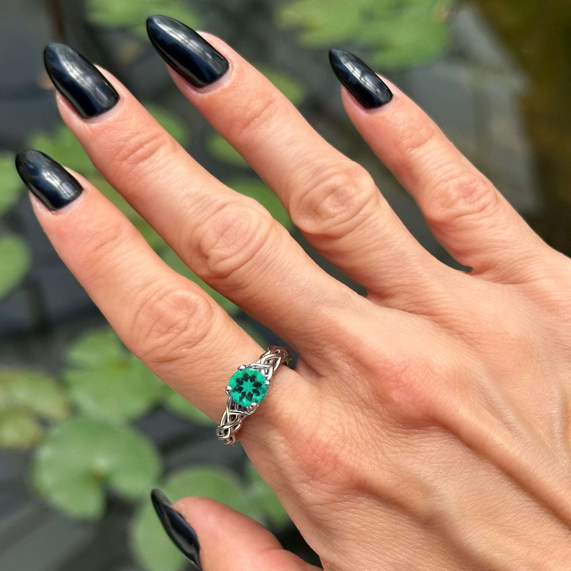 יד של אישה עם לק שחור שעונדת טבעת אירוסין אמרלד