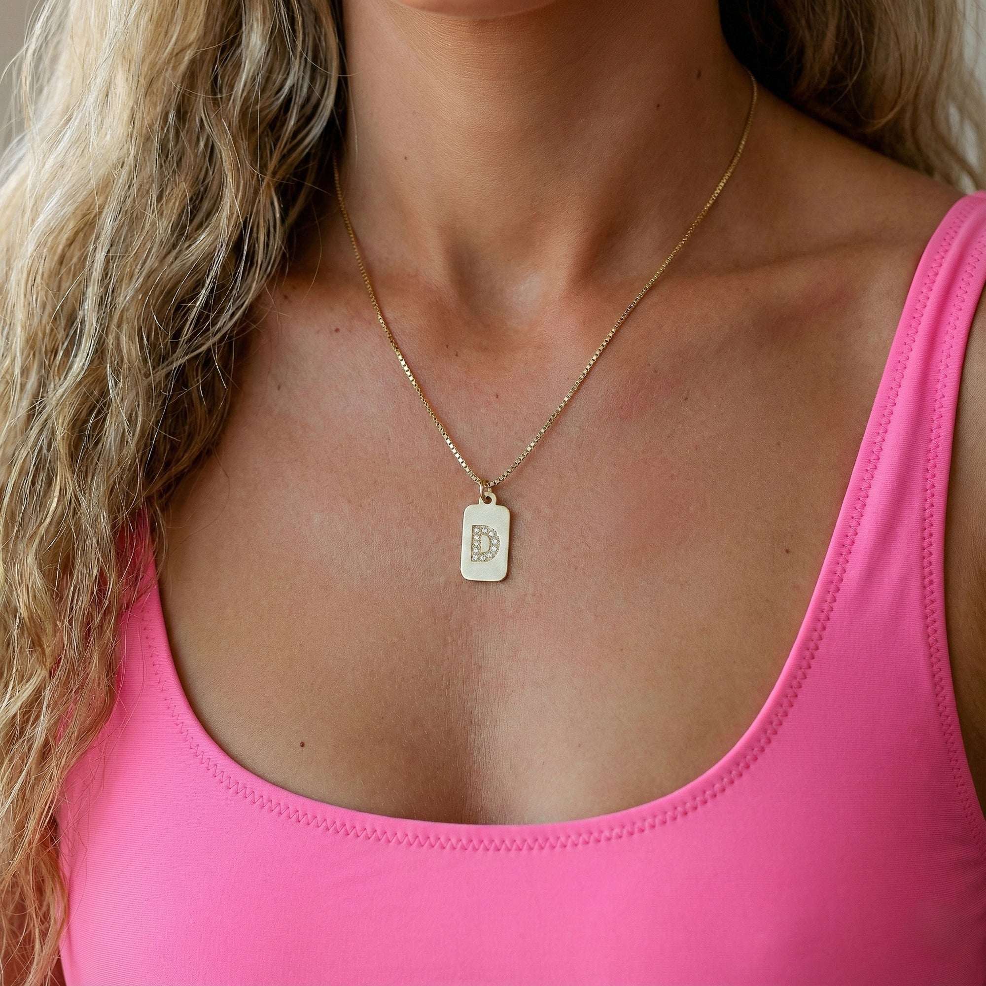 אישה עם חולצה ורודה ושרשרת עם שרשרת זהב ותליון אות באנגלית