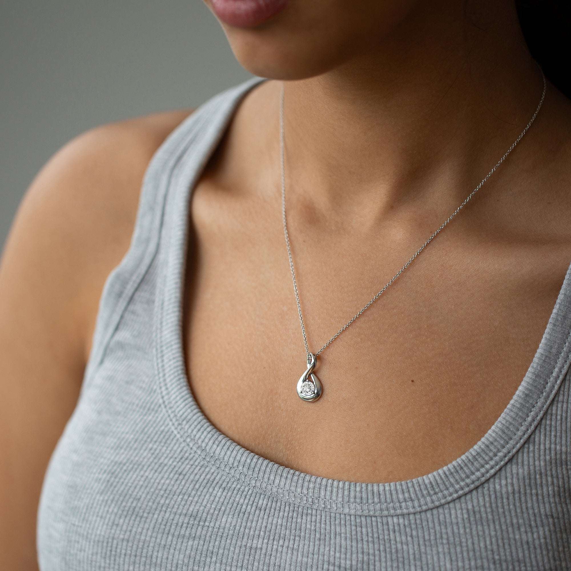 אישה עונדת שרשרת זהב לבן עם תליון משובץ יהלום וגופיה אפורה