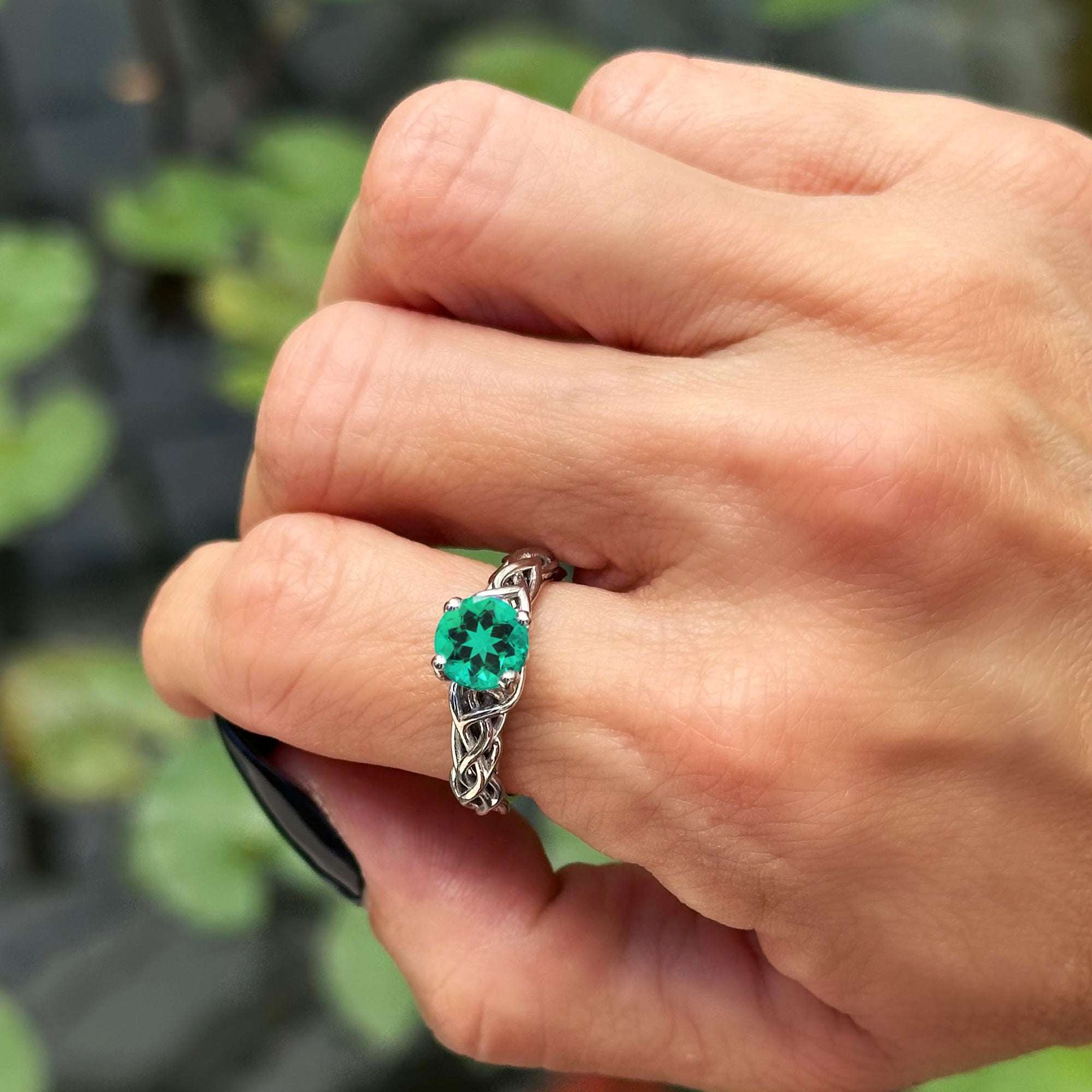 תקריב של יד של אישה שעונדת טבעת זהב אמרלד עם רקע מטושטש