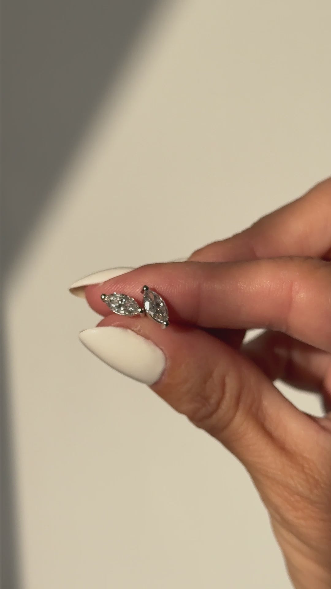 אצבעות מחזיקות  עגילי יהלום מעבדה בחיתוך מרקיזה על רקע אפור 