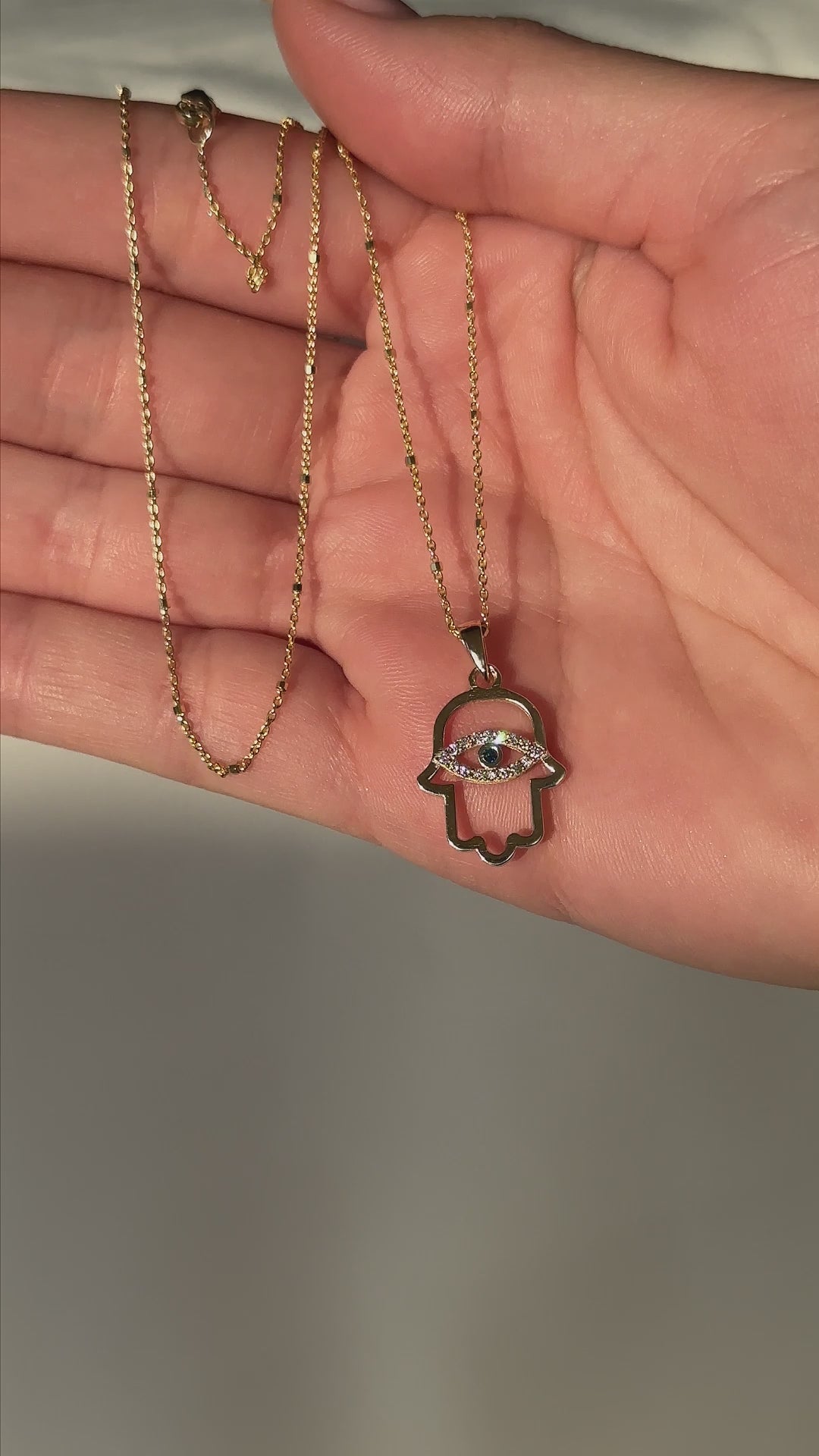 יד של אישה מחזיקה שרשרת חמסה זהב משובצץ יהלומים בעיצוב עין הרע