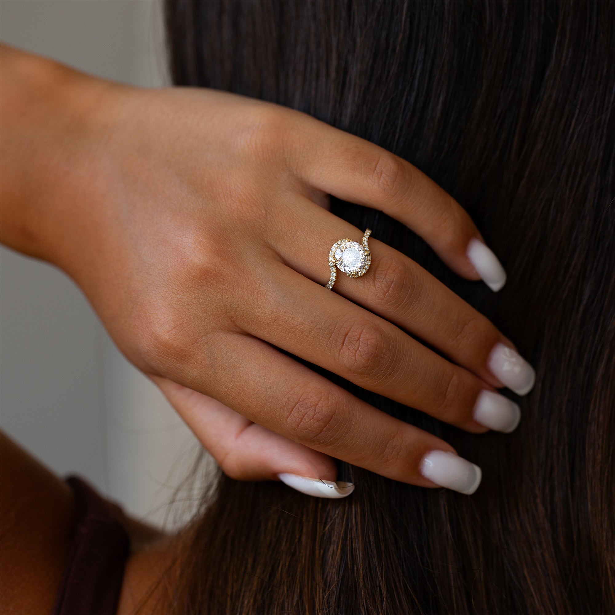 יד של אישה שעונדת טבעת מוסונייט משובצת יהלומי מעבדה, מחזיקה את ידה על שיערה