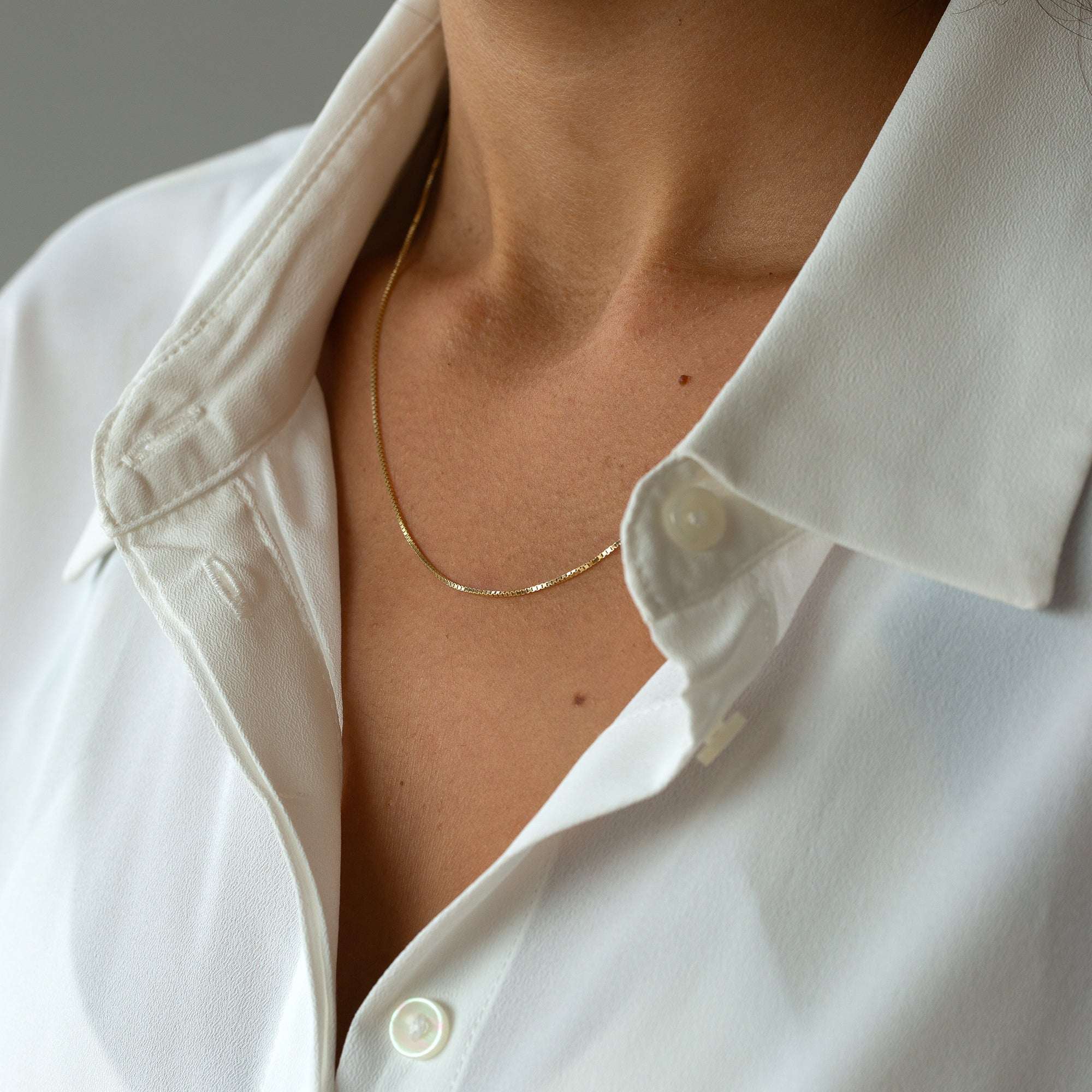 מבט מהצד על שרשרת זהב עדינה המציג את האופן שבו הזהב נח על קו הצוואר.